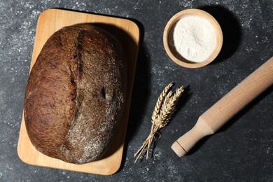 Photo of Loaf of fresh bread, flour and rolling pin on grey textured table, flat lay