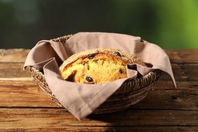 Photo of Loaf of fresh bread with sesame seeds and raisins in wicker basket on wooden table against blurred background, closeup