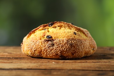 Photo of Loaf of fresh bread with sesame seeds and raisins on wooden table against blurred background, closeup