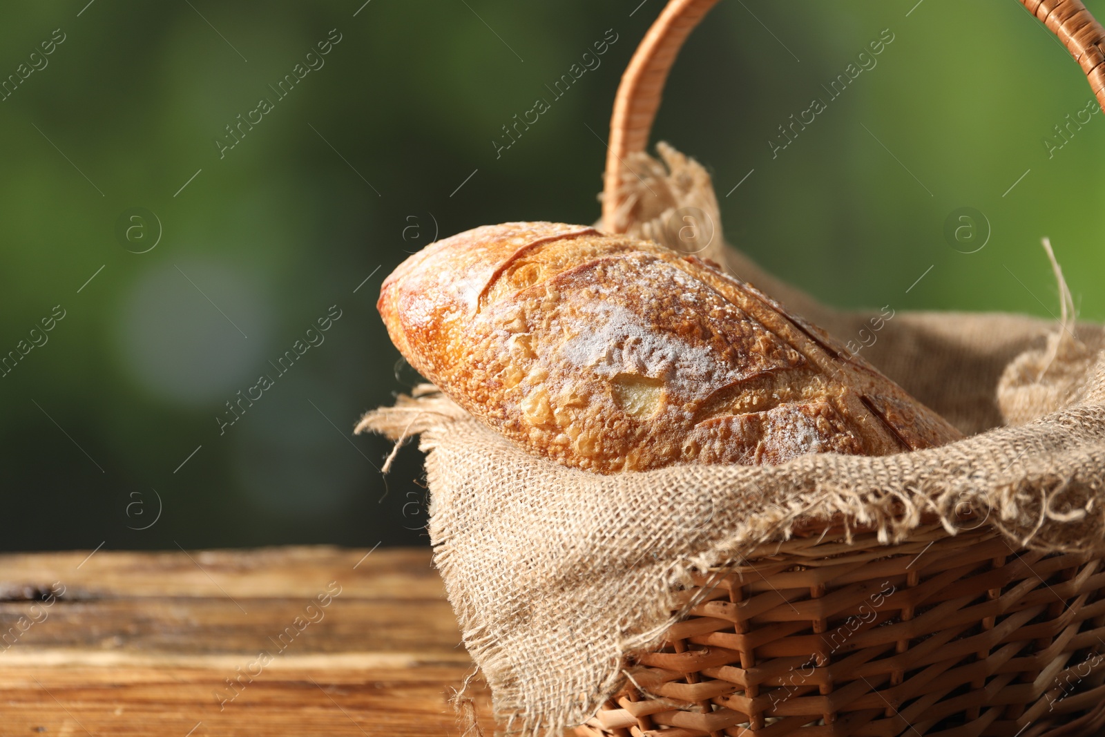 Photo of Loaf of fresh bread in wicker basket on wooden table against blurred background, closeup. Space for text