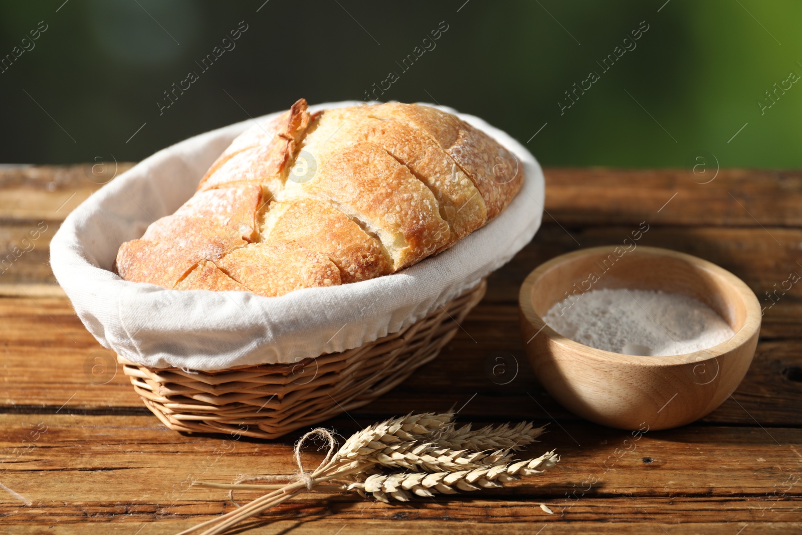 Fresh cut bread in wicker basket, flour and spikelets on wooden table against blurred background, closeup Photo of Fresh cut bread in wicker basket, flour and spikelets on wooden table against blurred background, closeup