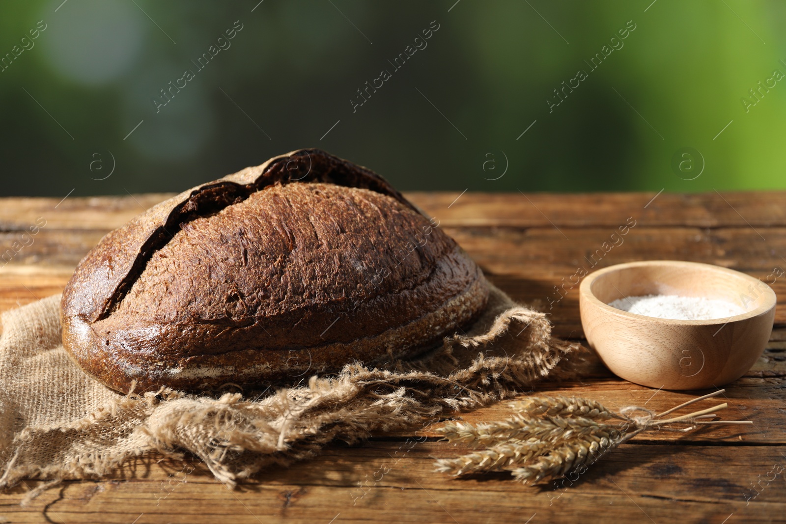 Loaf of fresh bread, flour and spikelets on wooden table against blurred background, closeup Photo of Loaf of fresh bread, flour and spikelets on wooden table against blurred background, closeup