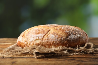 Photo of Loaf of fresh bread on wooden table against blurred background, closeup