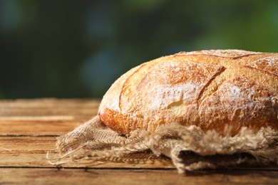 Photo of Loaf of fresh bread on wooden table against blurred background, closeup. Space for text