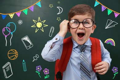 Image of Amused child in eyeglasses near green chalkboard with drawings