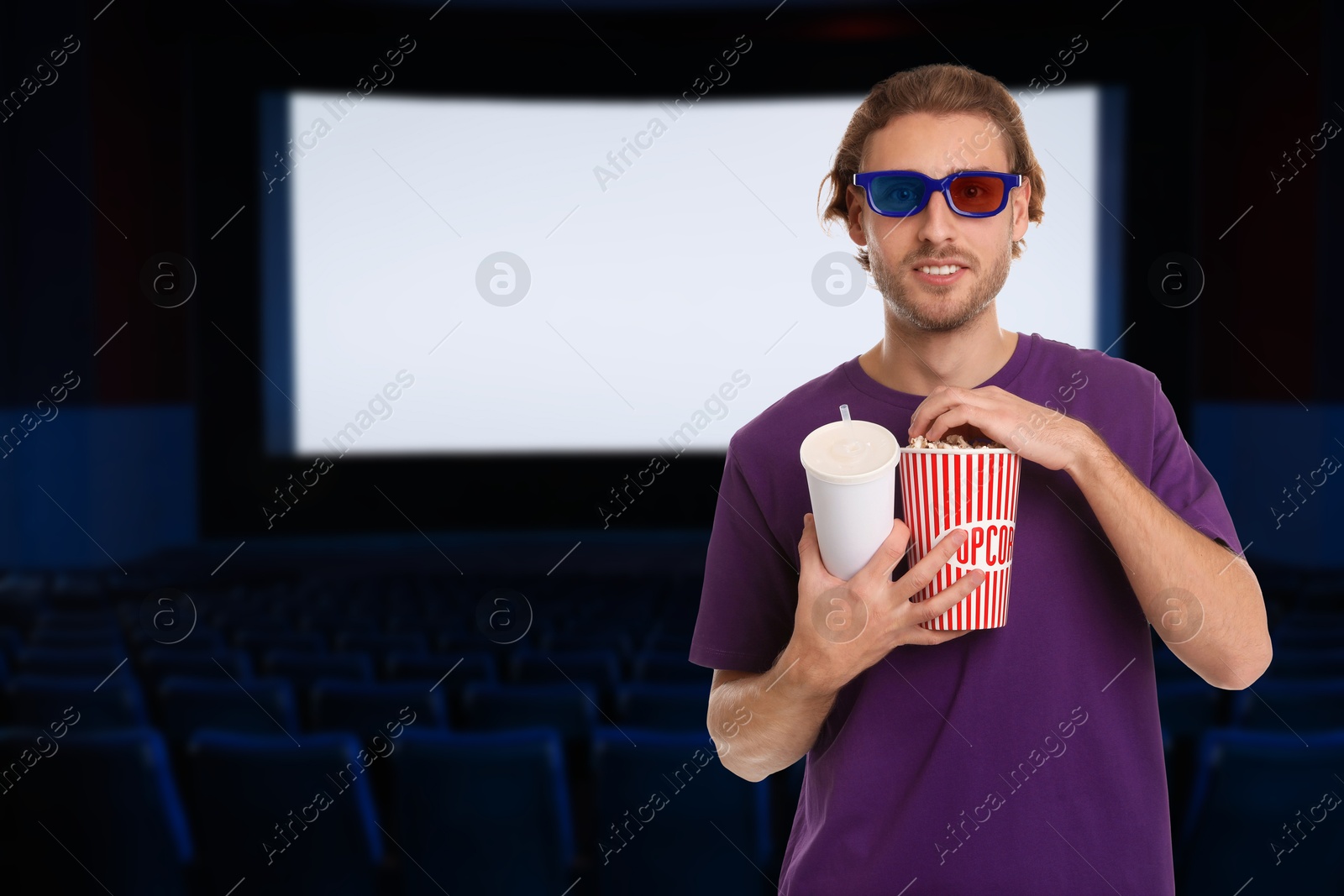 Image of Man with 3D glasses, beverage and popcorn in dark cinema