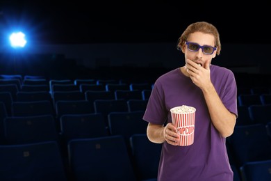 Image of Man with 3D glasses eating popcorn in dark cinema