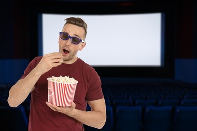 Image of Man with 3D glasses eating popcorn in dark cinema