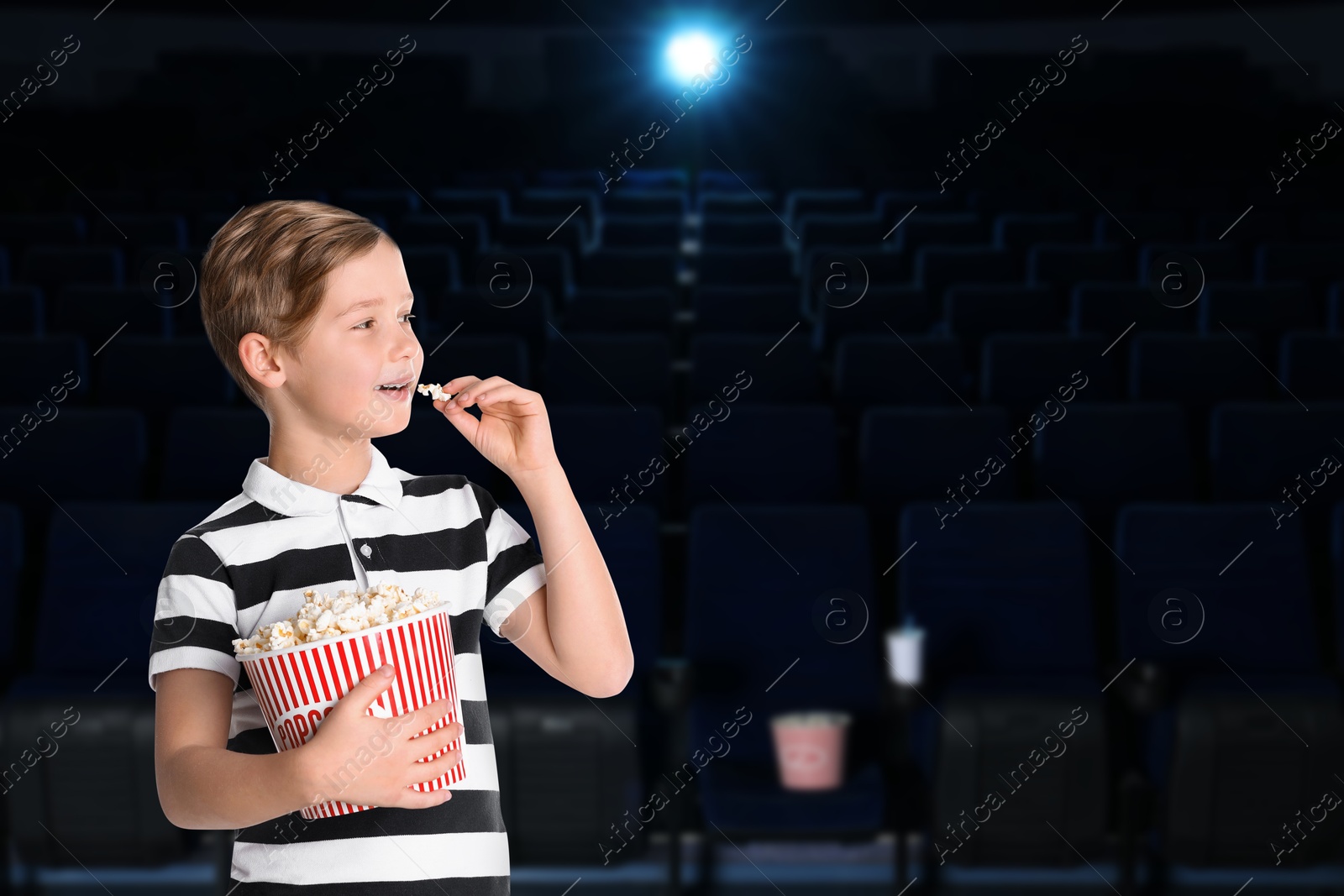 Image of Little boy eating popcorn in dark cinema