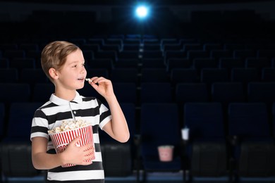 Image of Little boy eating popcorn in dark cinema