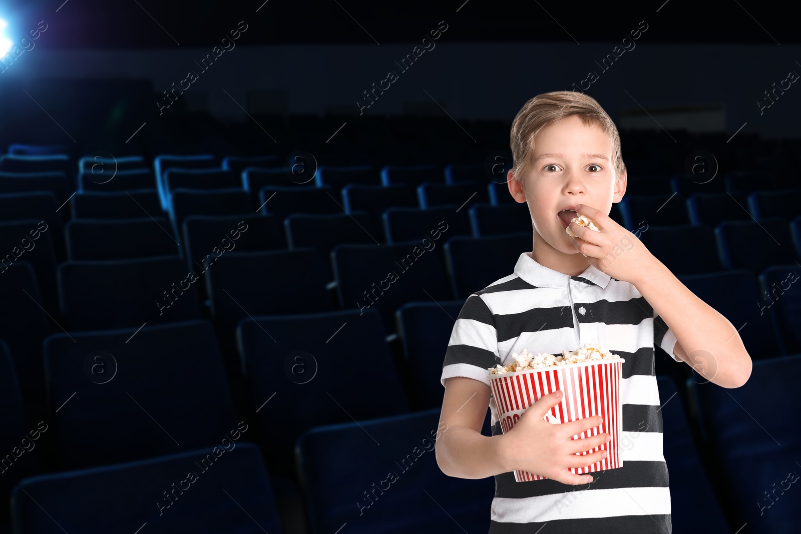 Image of Little boy eating popcorn in dark cinema