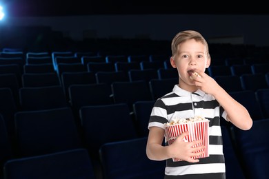 Image of Little boy eating popcorn in dark cinema