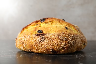 Photo of Loaf of fresh bread with sesame seeds and raisins on black marble table, closeup