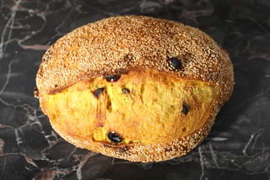 Photo of Loaf of fresh bread with sesame seeds and raisins on black marble table, above view