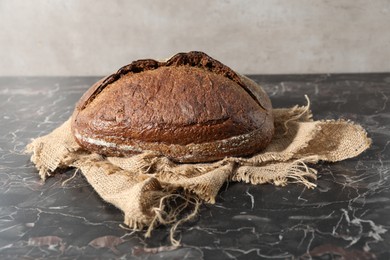 Photo of Loaf of fresh bread on black marble table, closeup