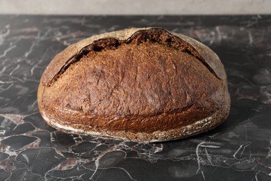 Photo of Loaf of fresh bread on black marble table, closeup