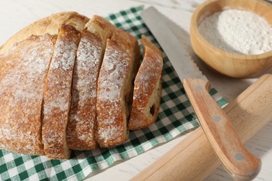 Photo of Loaf of fresh bread, flour, knife and rolling pin on white wooden table, closeup