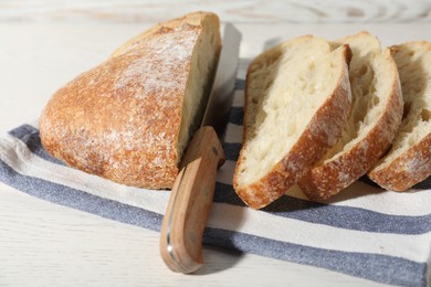Photo of Loaf of fresh bread and knife on white wooden table, closeup