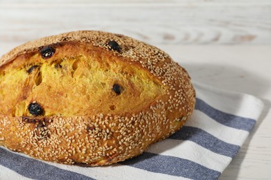 Photo of Loaf of fresh bread with sesame seeds and raisins on white wooden table, closeup