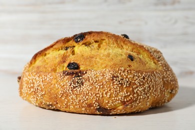 Photo of Loaf of fresh bread with sesame seeds and raisins on white wooden table, closeup