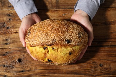 Photo of Baker with loaf of fresh bread at wooden table, top view