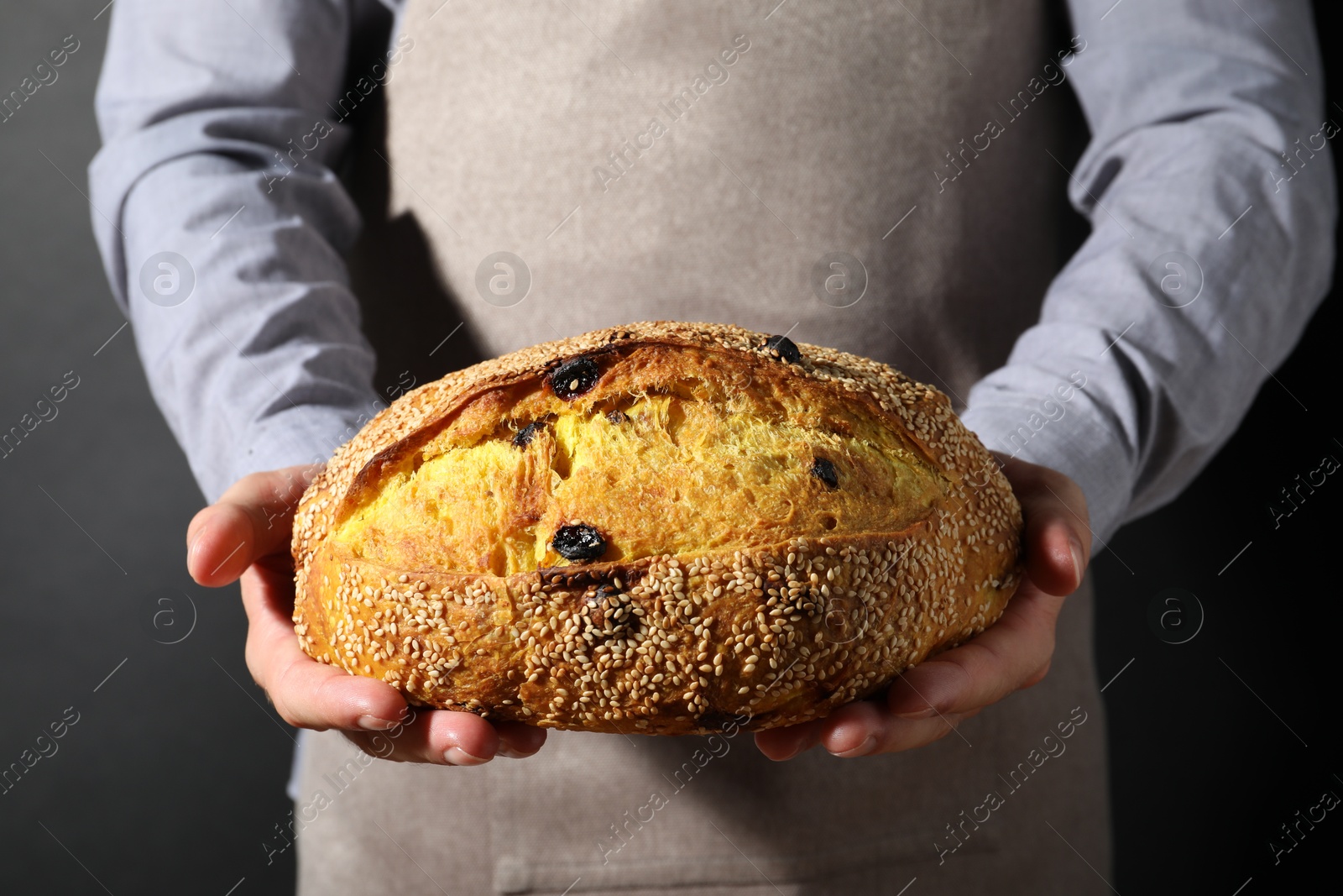Baker with loaf of fresh bread with sesame seeds and raisins on black background, closeup Photo of Baker with loaf of fresh bread with sesame seeds and raisins on black background, closeup