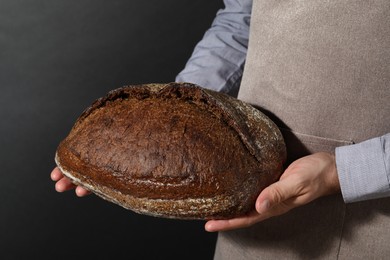 Photo of Baker with loaf of fresh bread on black background, closeup