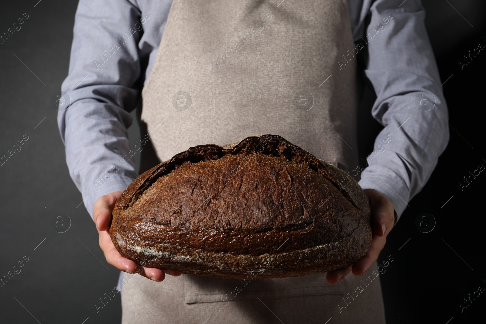 Photo of Baker with loaf of fresh bread on black background, closeup