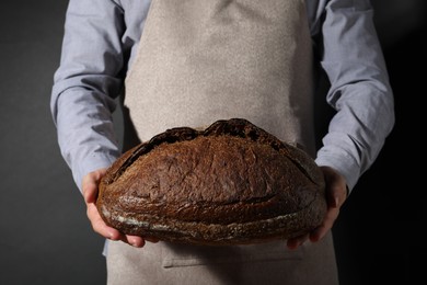 Photo of Baker with loaf of fresh bread on black background, closeup