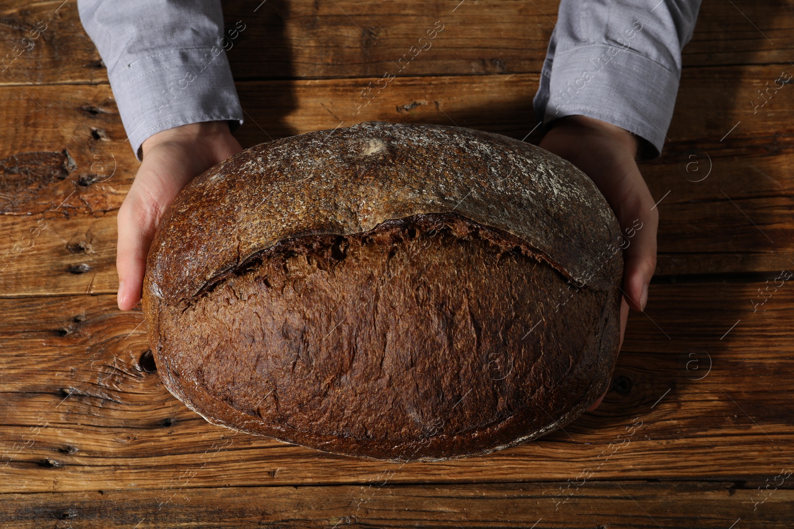 Baker with loaf of fresh bread at wooden table, top view Photo of Baker with loaf of fresh bread at wooden table, top view