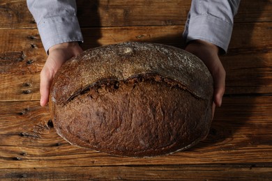 Photo of Baker with loaf of fresh bread at wooden table, top view