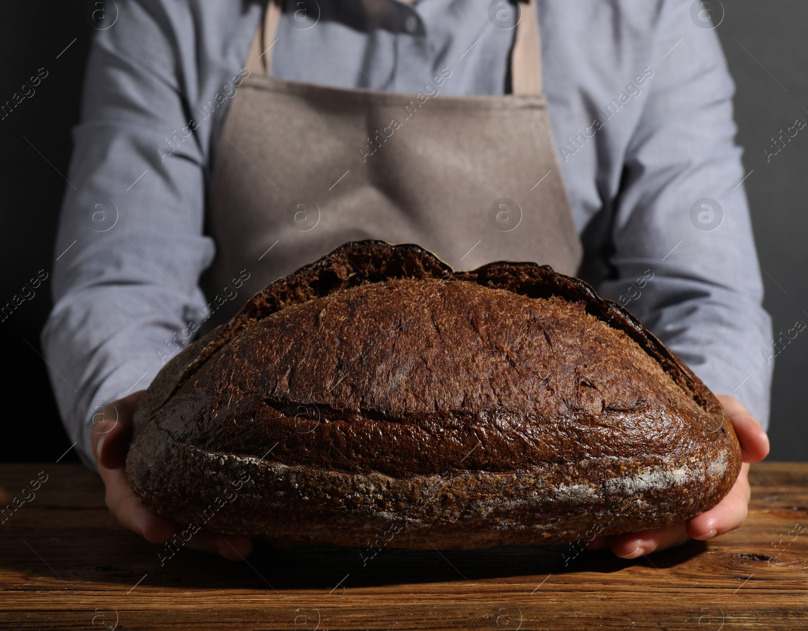 Baker with loaf of fresh bread at wooden table, closeup Photo of Baker with loaf of fresh bread at wooden table, closeup