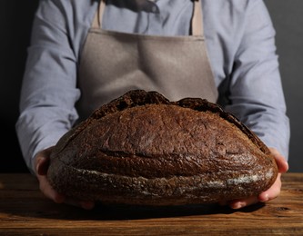 Photo of Baker with loaf of fresh bread at wooden table, closeup