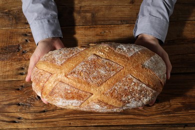 Photo of Baker with loaf of fresh bread at wooden table, top view