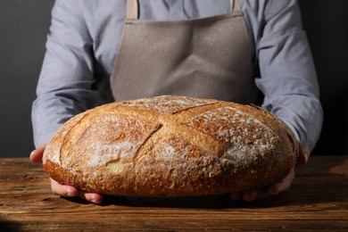 Photo of Baker with loaf of fresh bread at wooden table, closeup