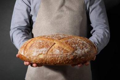 Photo of Baker with loaf of fresh bread on black background, closeup