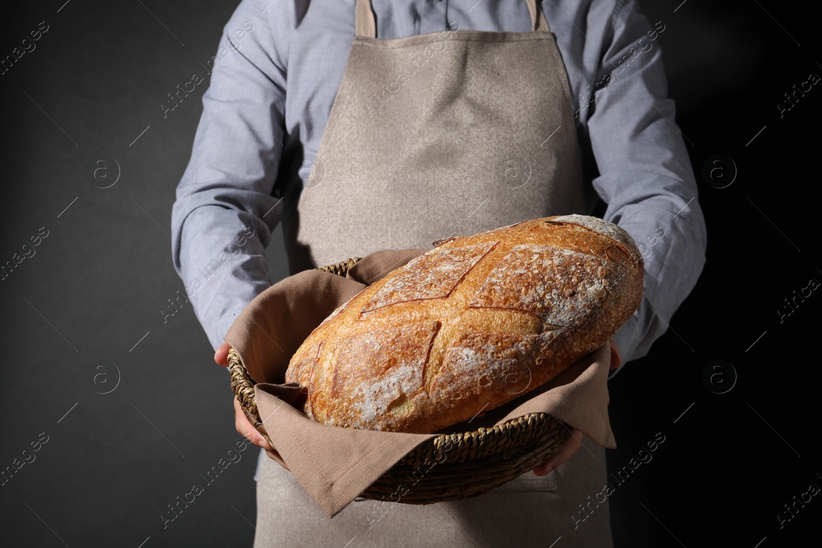 Photo of Baker with loaf of fresh bread on black background, closeup