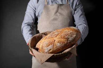 Photo of Baker with loaf of fresh bread on black background, closeup