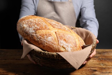 Photo of Baker with loaf of fresh bread in wicker basket at wooden table, closeup