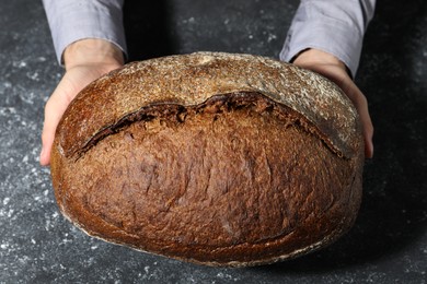 Photo of Baker with loaf of fresh bread at grey textured table, top view