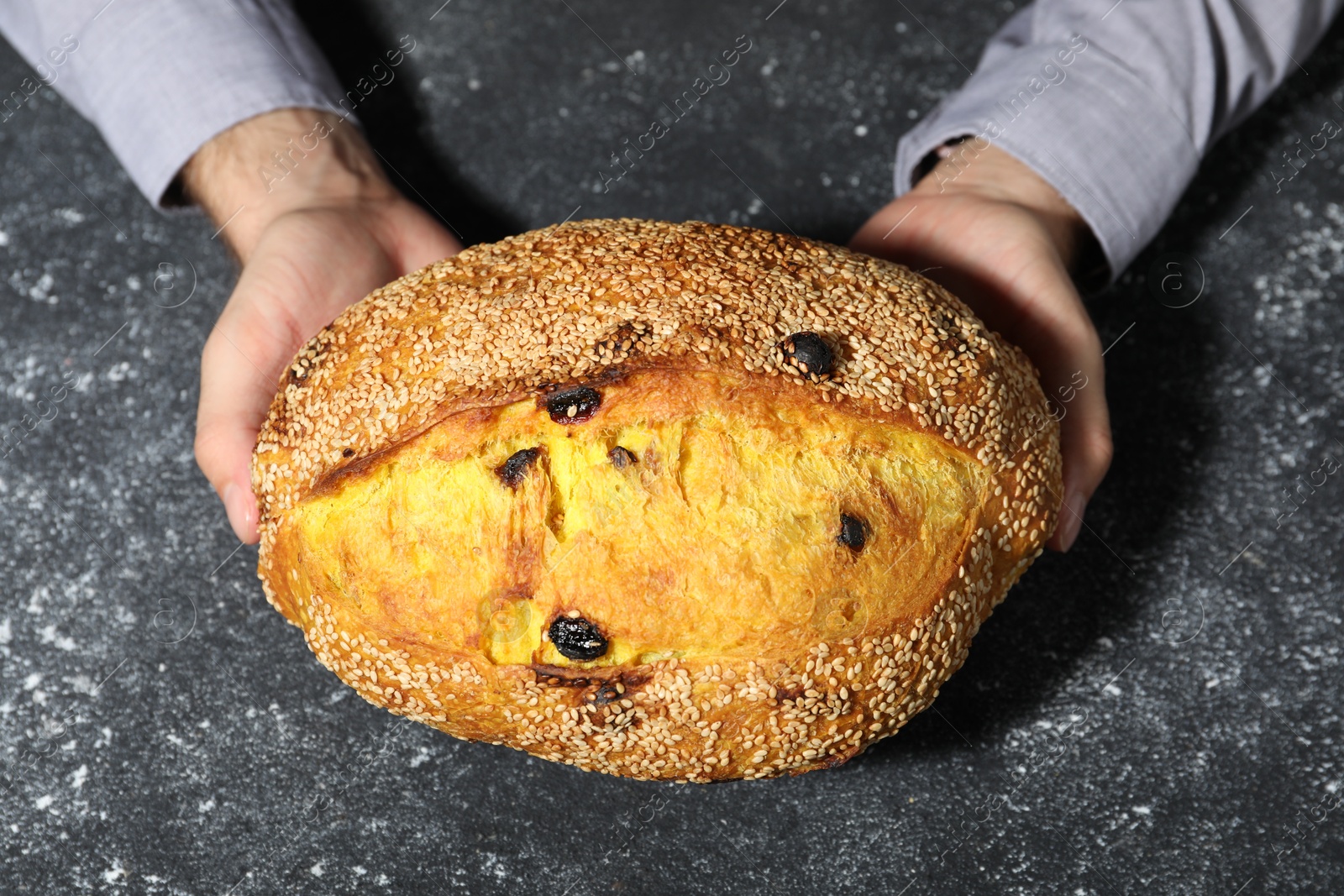 Photo of Baker with loaf of fresh bread at grey textured table, top view