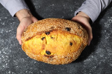 Photo of Baker with loaf of fresh bread at grey textured table, top view