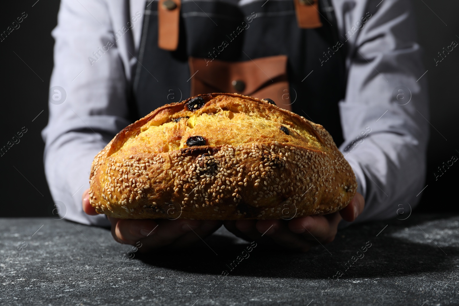 Photo of Baker with loaf of fresh bread at grey textured table, closeup