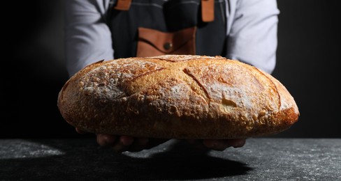 Photo of Baker with loaf of fresh bread at grey textured table, closeup