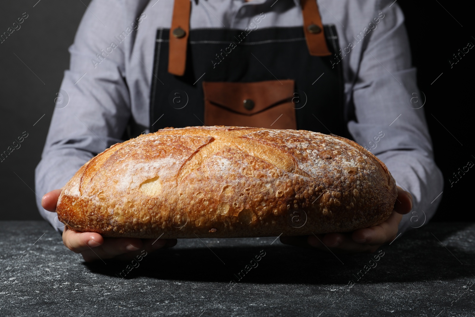 Photo of Baker with loaf of fresh bread at grey textured table, closeup