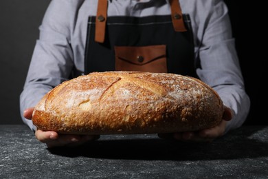 Photo of Baker with loaf of fresh bread at grey textured table, closeup