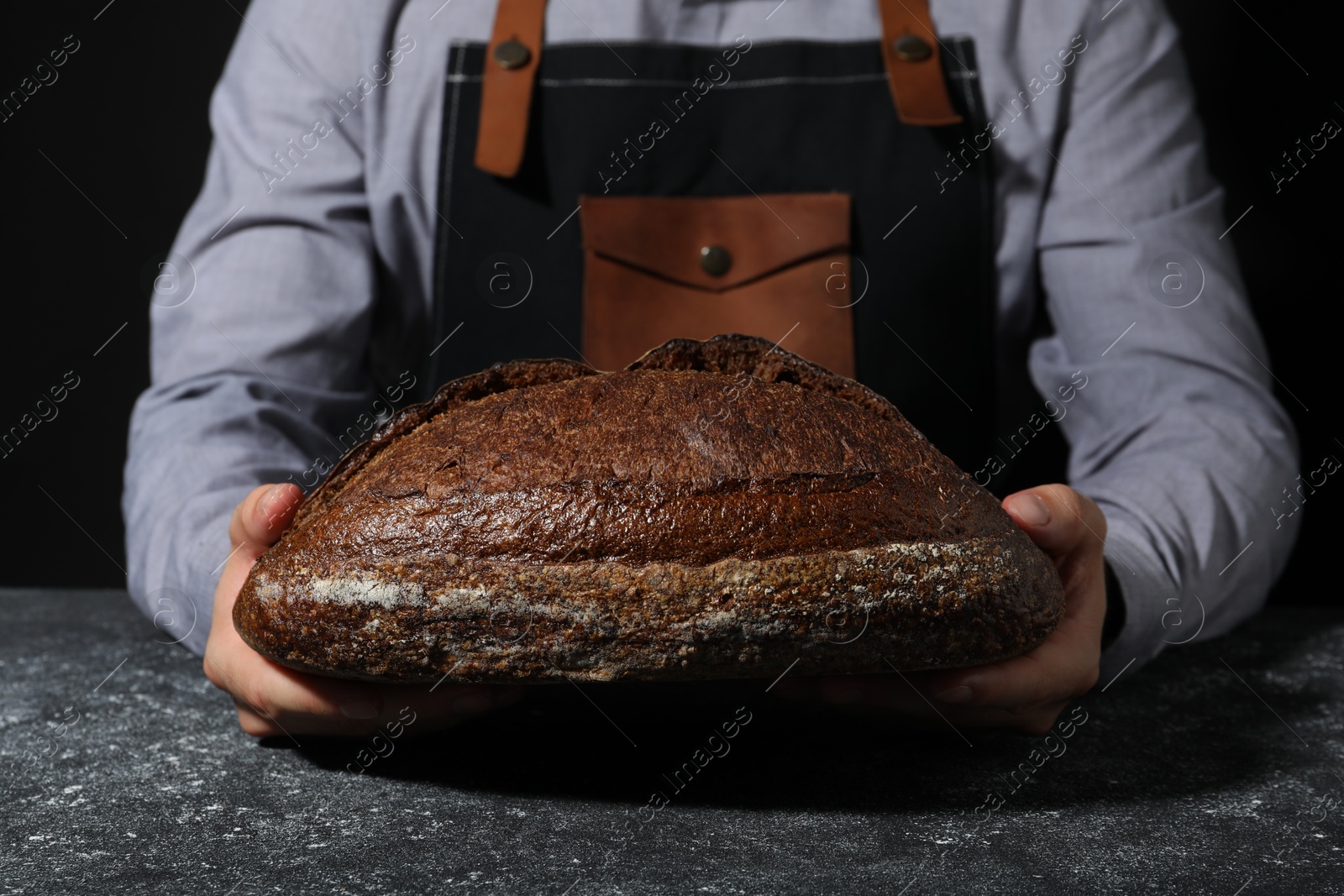 Photo of Baker with loaf of fresh bread at grey textured table, closeup