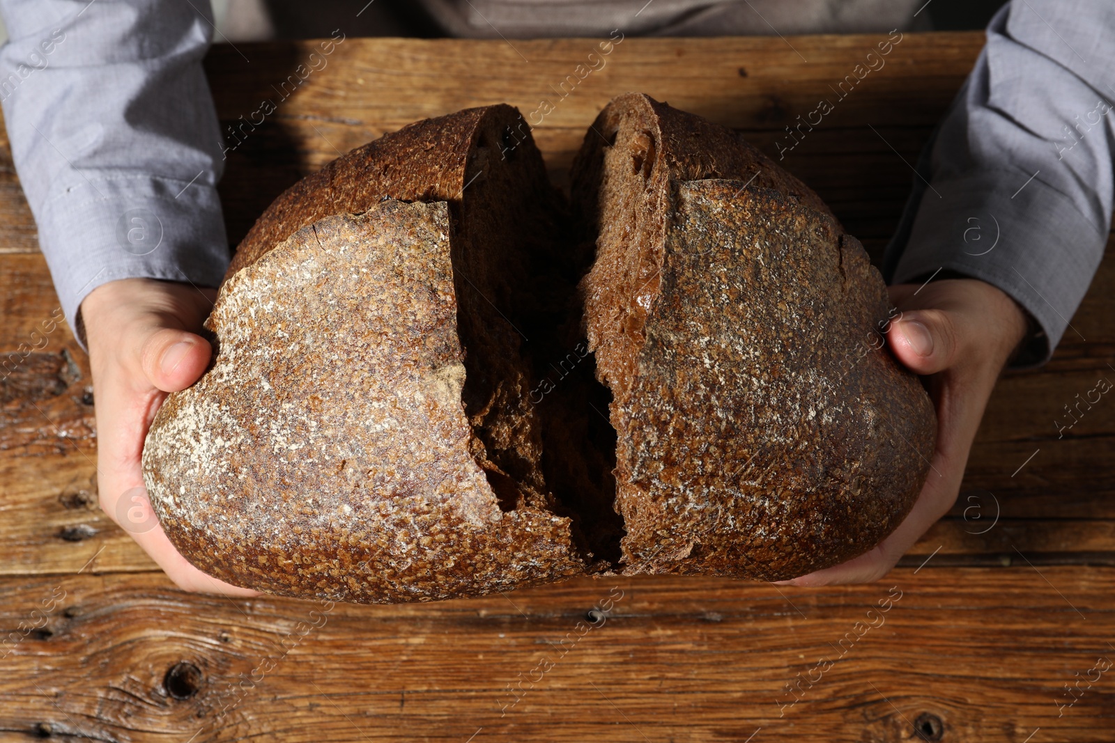 Photo of Baker breaking loaf of fresh bread at wooden table, top view
