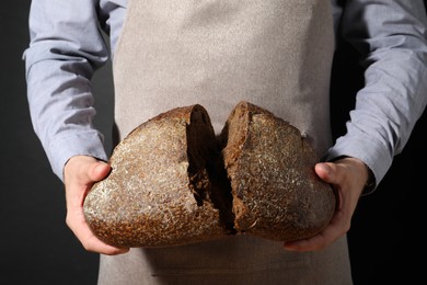 Photo of Baker breaking loaf of fresh bread on black background, closeup