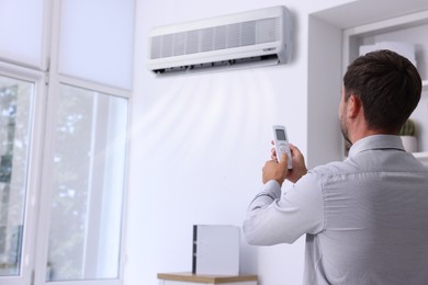 Image of Man switching on air conditioner with remote control in office